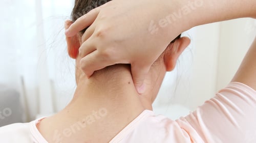 Preview: Back view of Asian woman using hands to massage the nape of her neck in physical therapy to reduce p