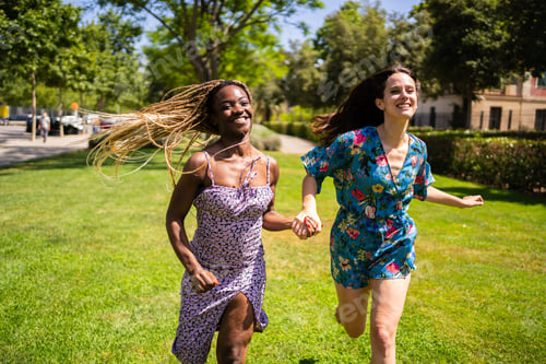 Preview: Two happy multiethnic women running holding hands outdoors