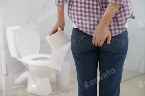 Preview: Woman with toilet paper suffering from hemorrhoid in rest room, closeup