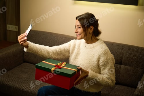 Preview: Pleased woman taking selfie on smartphone of herself with gift during Christmas