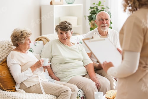 Preview: Happy elders sitting on a couch while talking to a nurse