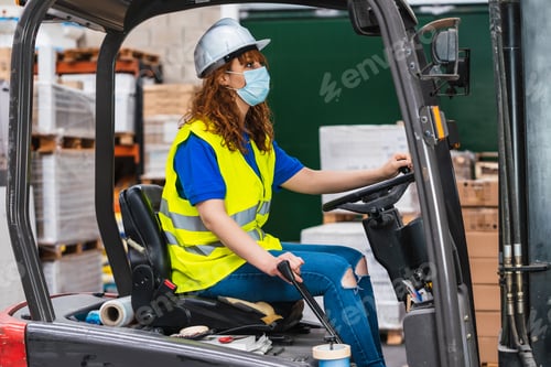 Preview: Industrial female worker wearing a medical mask using a loader in a warehouse