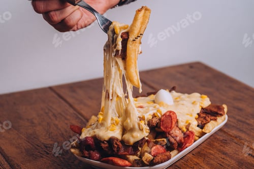 Preview: Closeup shot of a dish with french fries, sausages topped with cheese and corn on a wooden table.