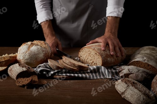 Preview: cropped image of baker in apron cutting bread on sackcloth on wooden table