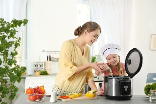 Preview: Mother and daughter preparing food with modern multi cooker in kitchen