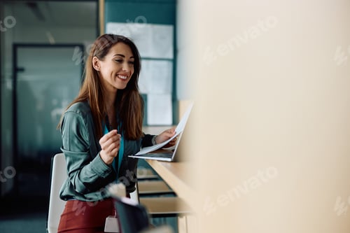 Preview: Young businesswoman using laptop and analyzing reports while working in the office.