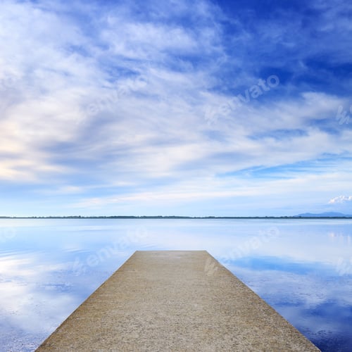 Preview: Concrete pier or jetty and on a blue lake and sky reflection on water.