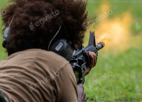 Preview: Female with curly hair lying on the grass with a paintball weapon