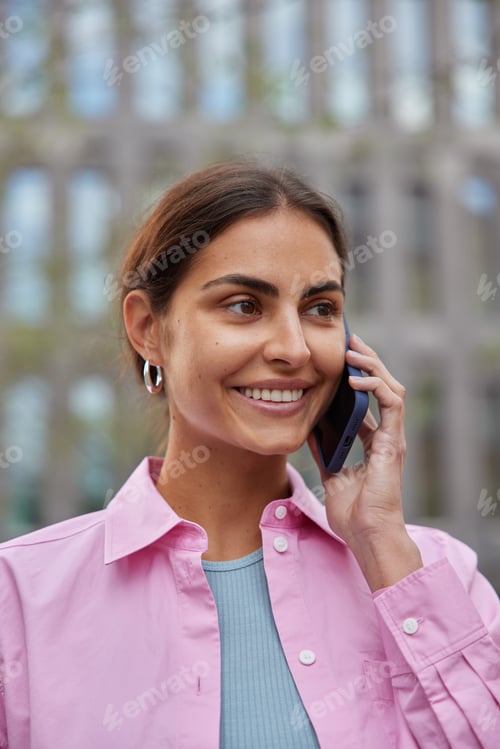 Preview: Vertical shot of positive young European woman with dark combed hair feels glad enjoys cellphone con