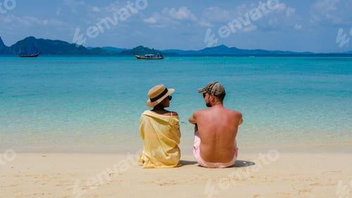 Preview: the backside of a couple of men and women sitting at the beach of Koh Kradan island in Thailand