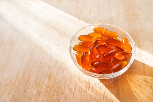 Preview: Lecithin gel pills in a round glass bowl with sun light on wooden background. Soy and sunflower