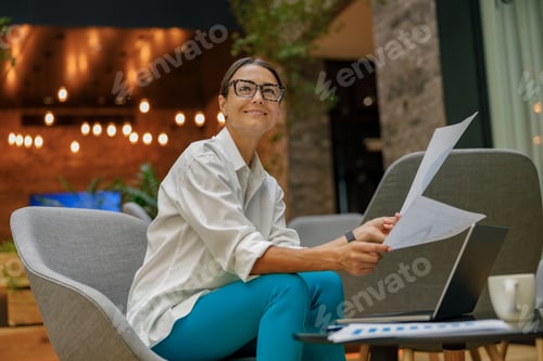 Preview: Positive female analyst working with documents and use laptop while sitting in modern coworking