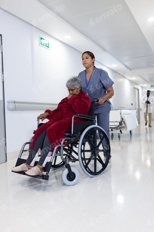 Preview: Asian female doctor pushing diverse senior female patient in wheelchair in hospital corridor