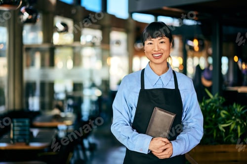 Preview: Portrait of a smiling Asian waitress, holding a bill case.