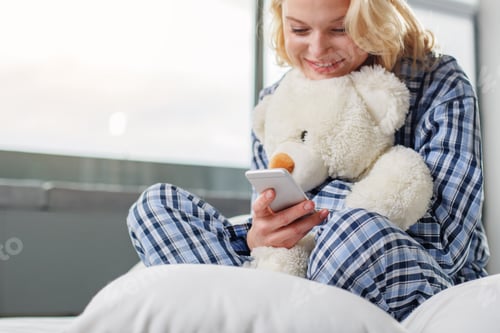 Preview: Low Angle Portrait Of Shiny Blond Taking Rest At Home. She Is Holding Soft Toy And Mobile Phone