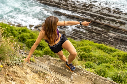 Preview: Sportswoman walking down stone stairs and pointing at flysch cliffs of zumaia
