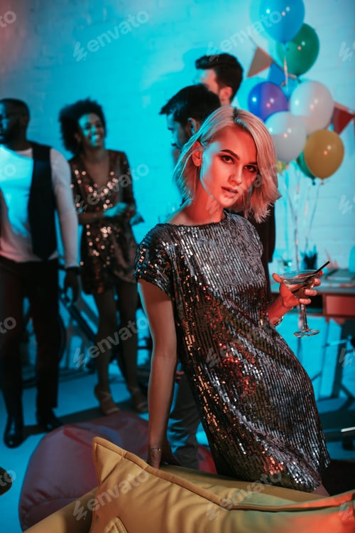 Preview: Glamorous woman holding glass with cocktail by friends at party