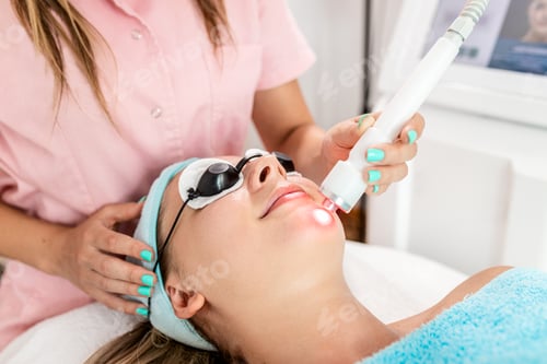 Preview: Beautician therapist applying face treatment in beauty salon to young woman.