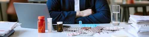 Preview: Header of Man Sitting at Desk Surrounded by Various Medications