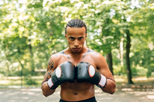 Preview: Close up portrait of a sweated kickboxer with gloves and mouth guard looking at the camera