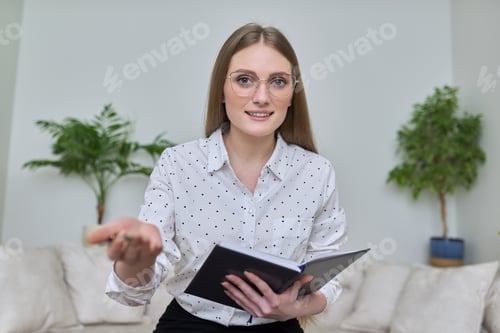 Preview: Smiling Woman Extends Hand Holding Book Indoors