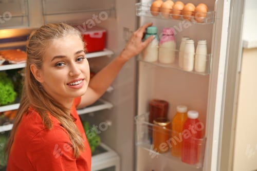 Preview: Young woman taking yogurt from refrigerator at home