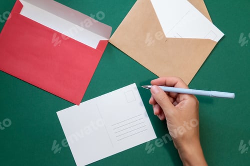 Preview: Hand writing on greeting postcard, envelopes on green background