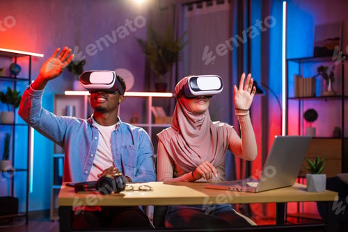 Preview: Diverse couple sitting at desk in VR glasses playing games
