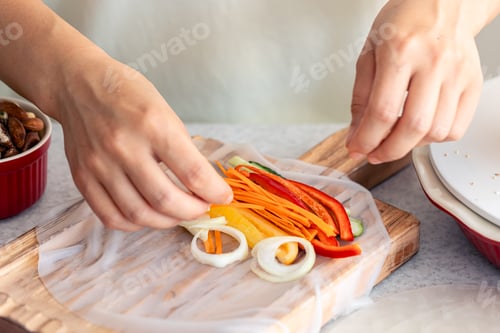 Preview: Woman preparing spring rolls in rice paper on kitchen table.