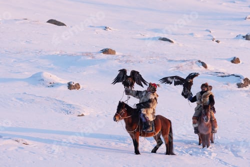 Preview: Two Mongolian eagle hunters ride horseback through a snowy landscape