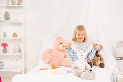 Preview: smiling cute child playing with soft toys in bed
