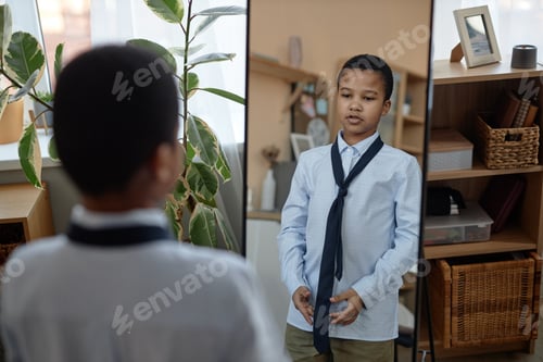 Preview: Young boy tying tie and looking in mirror