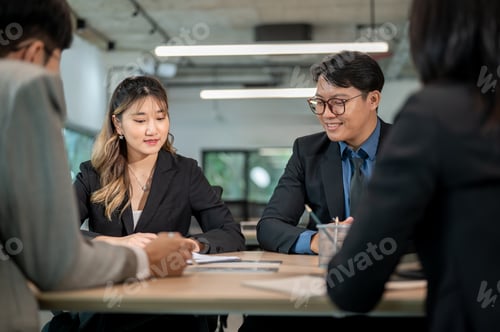 Preview: Businesswoman and male coworkers looking at document on clipboard at wooden table in a meeting room