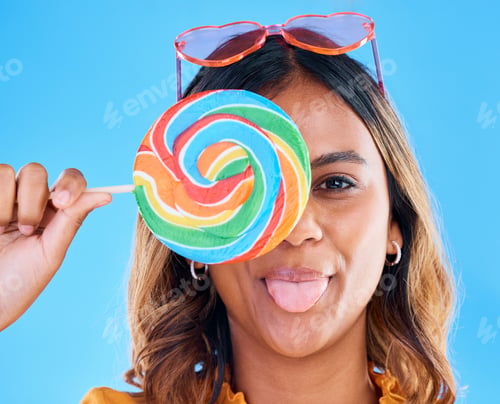Preview: Portrait, lollipop and tongue with a woman on a blue background in studio wearing heart glasses for