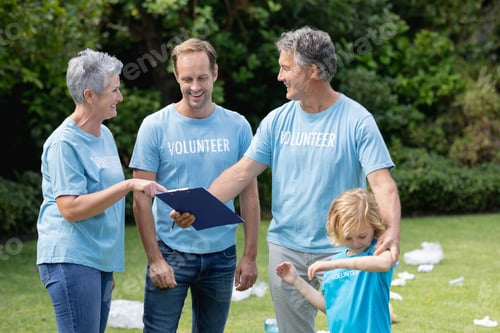 Preview: Caucasian senior couple with clipboard and man and son in volunteer shirts talking in littered field