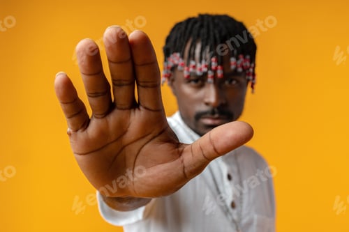 Preview: Portrait of serious African male showing hand stop sign on yellow background