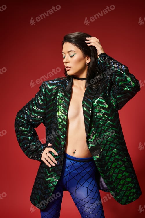 Preview: sexy asian woman in trendy green jacket with sequins posing with hand on hip on red backdrop