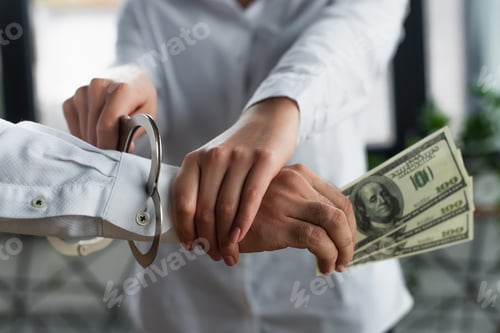 Preview: KYIV, UKRAINE - SEPTEMBER 22, 2021: partial view of woman putting handcuffs on man with dollars,