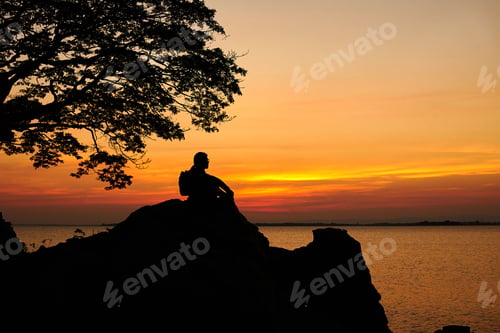 Preview: Silhouette scene of a woman sitting on a big rock on the beach