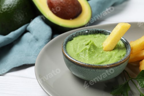 Preview: Plate with french fries, guacamole dip, parsley and avocado served on white wooden table, closeup