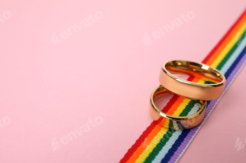 Preview: Wedding rings and rainbow ribbon on color background, space for text. Gay symbol