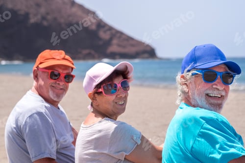 Preview: Rear view of three friends sitting on the beach, retired adult people in outdoor vacation at sea
