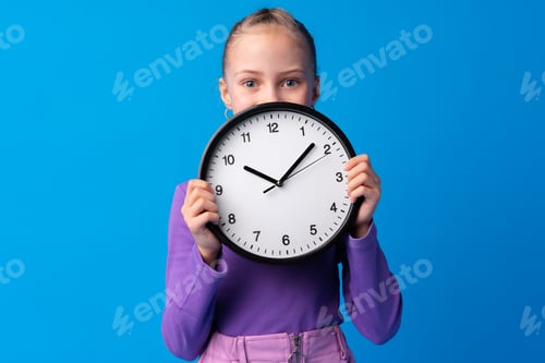 Preview: Beautiful teen girl holding wall clock over blue background
