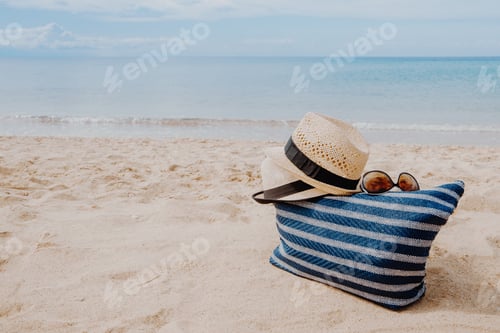 Preview: Blue beach bag with sunglasses and hats on the sandy beach with the blue sky background