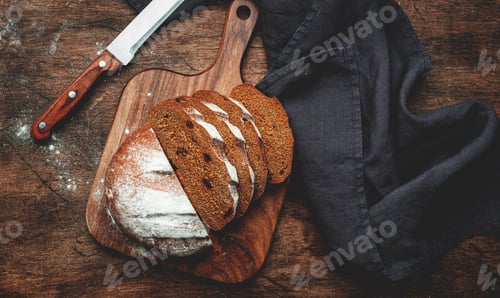 Preview: Sourdough rye bread with raisins, pieces on wooden cutting board, bread knife and kitchen towel