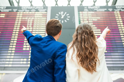 Preview: Young couple in international airport looking at the flight information board