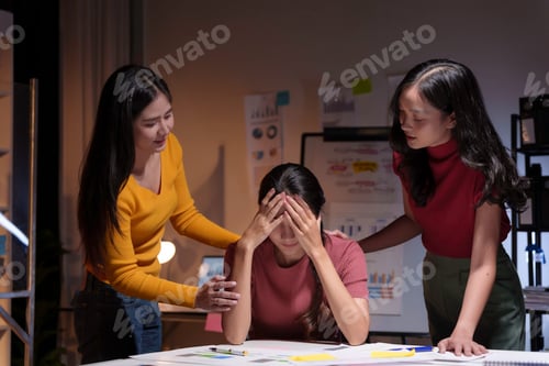 Preview: Two young businesswomen comforting a stressed colleague while working late in their office at night