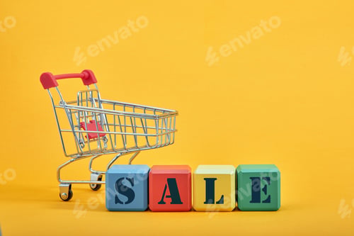 Preview: A miniature shopping cart and multi-colored cubes on yellow background. Sales word written on cubes.