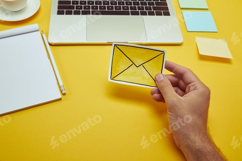 Preview: cropped image of man holding envelope sign near laptop