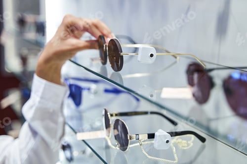 Preview: Female hand taking sunglasses from shelf in optical store